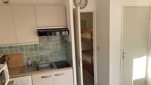 Cocina compacta con lavadora, microondas y lavamanos. Se ve una cama litera en la habitación contigua.