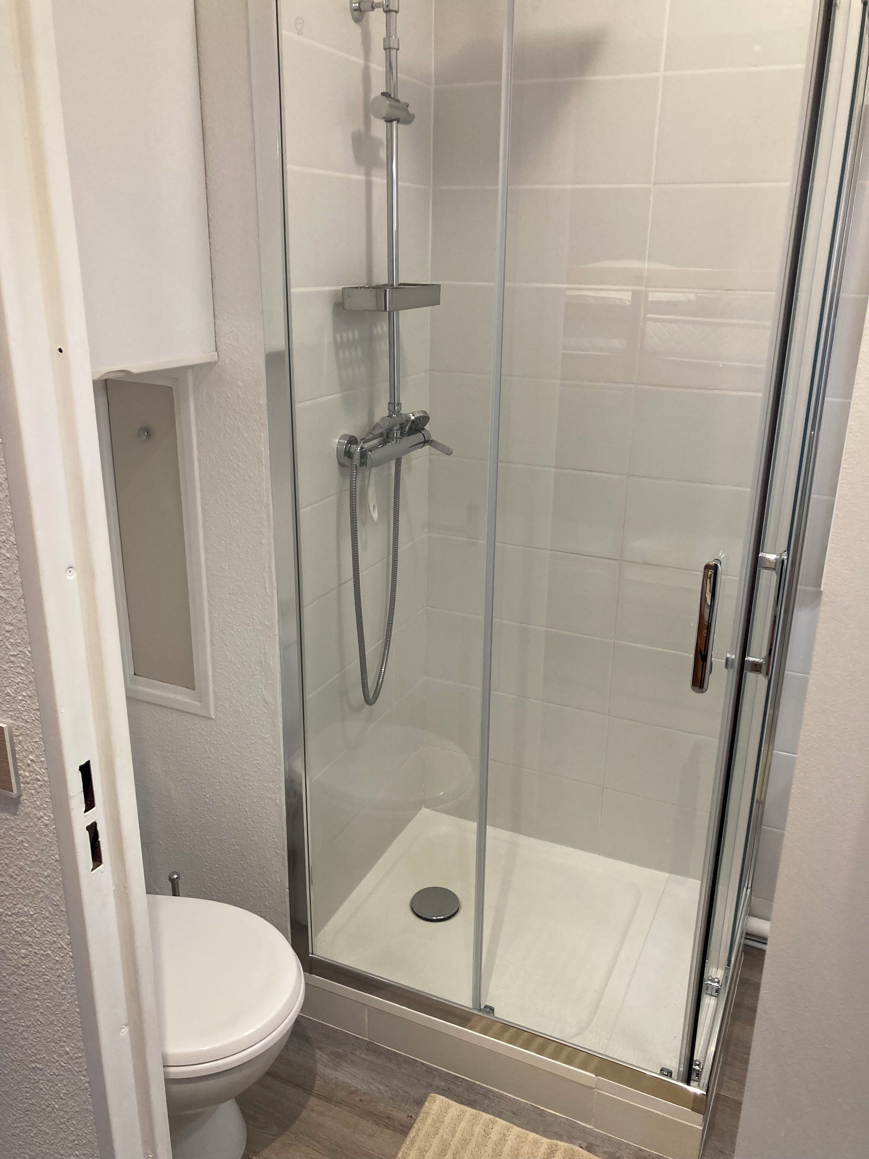 Eine Duschkabine mit Glaswänden, einer Handbrause und einem am Wand montierten Wasserhahn.
