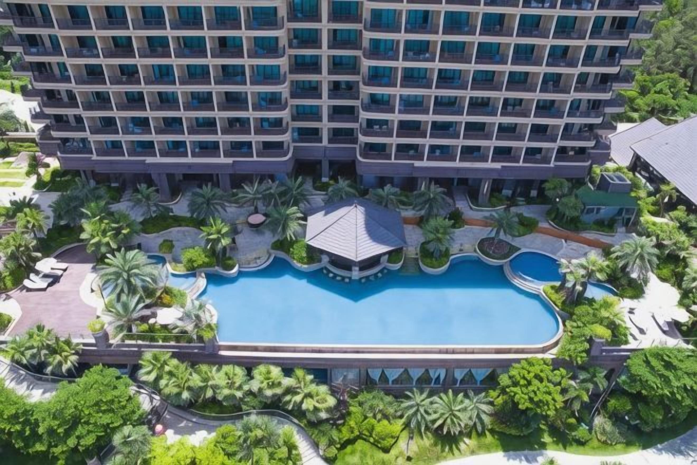 Hotel de varios pisos con piscina central rodeada de palmeras y vegetación.