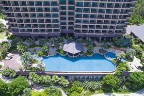 A multi-story hotel with a central swimming pool surrounded by palm trees and greenery. - Huidong Shuangyue Bay Rainbow Bay Sea View Hotel (Huidong)