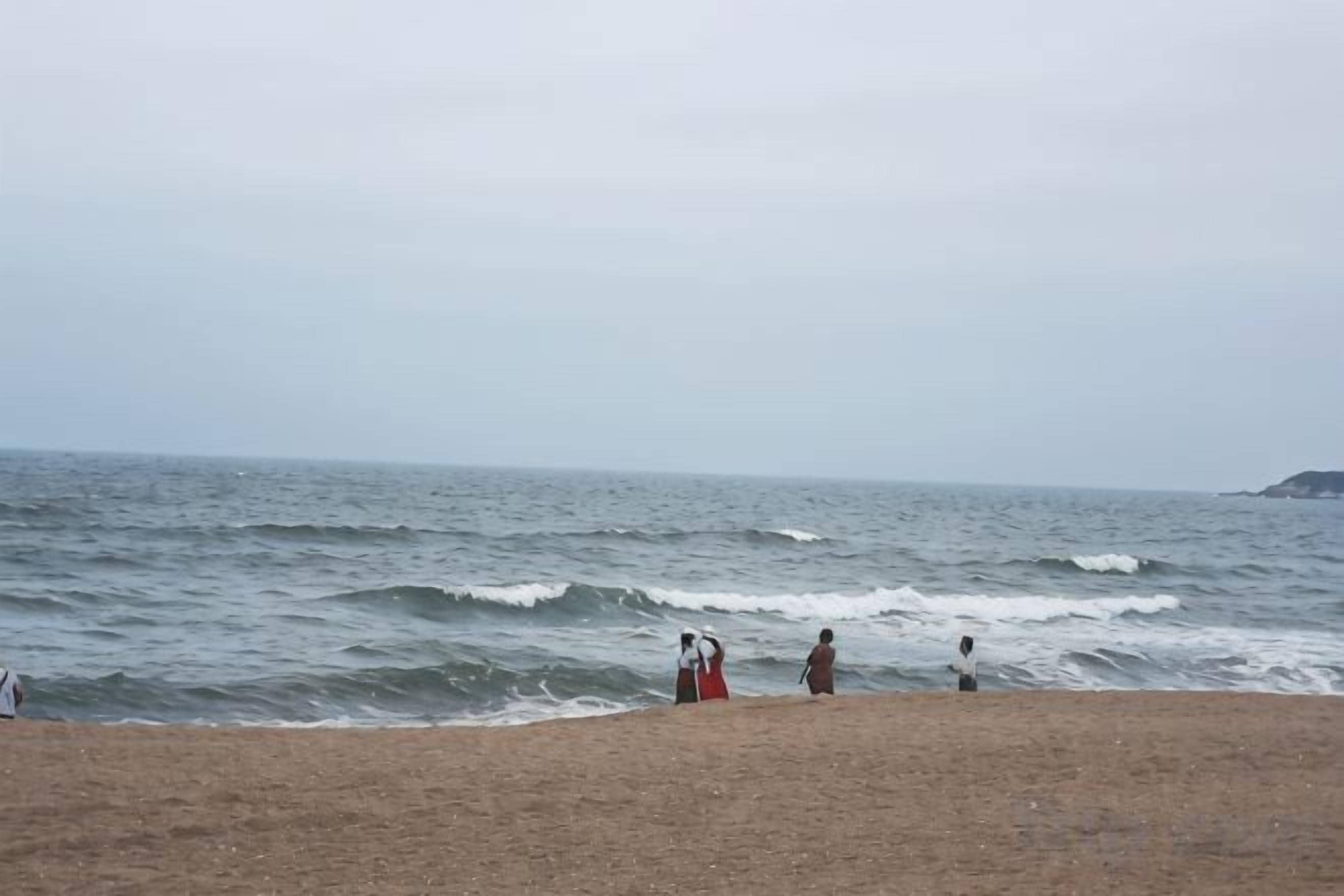Een strand met golven, een zandstrand en een landmassa in de verte.