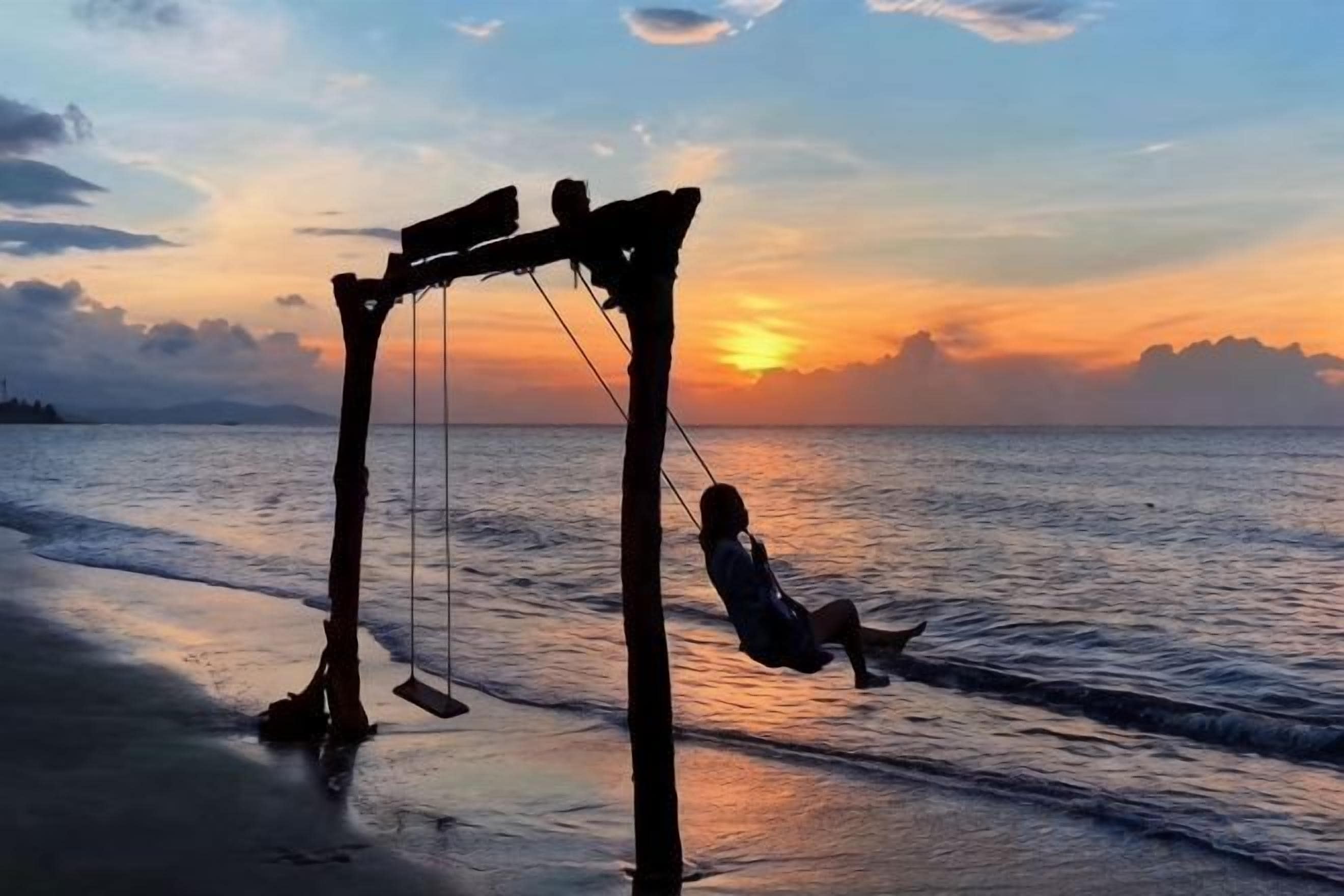 Un columpio en la playa, con el océano y la puesta de sol al fondo.