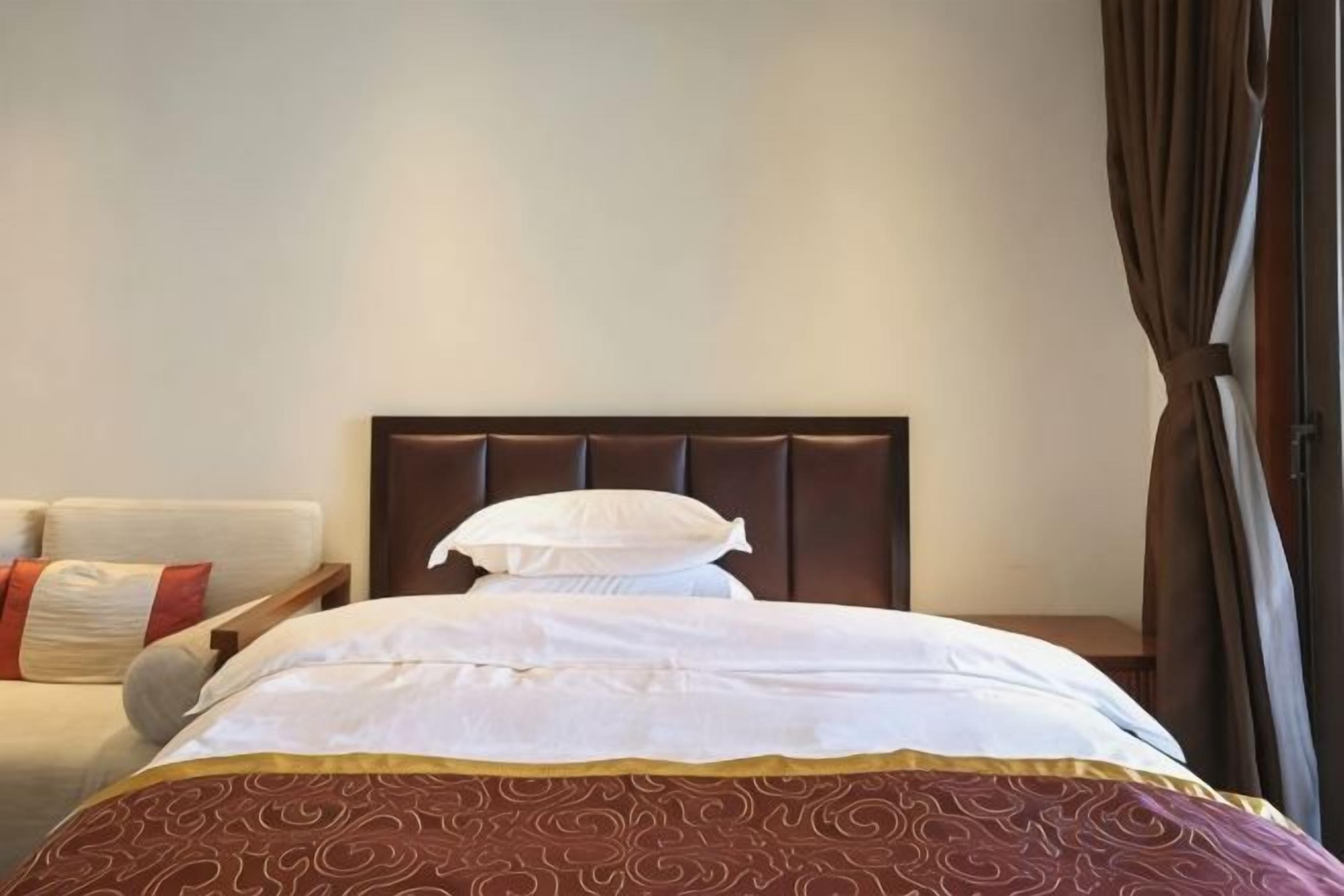 A hotel room with a bed, a nightstand, and a window with curtains.