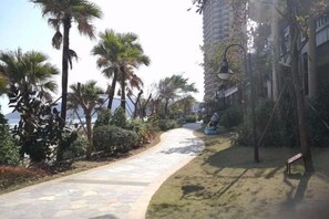 A pathway lined with palm trees and a bench, leading to a building with a visible balcony. - Huidong Shuangyue Bay Rainbow Bay Sea View Hotel (Huidong)