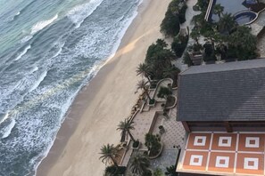 Un hotel frente a la playa con una arena dorada, olas del océano y palmeras.