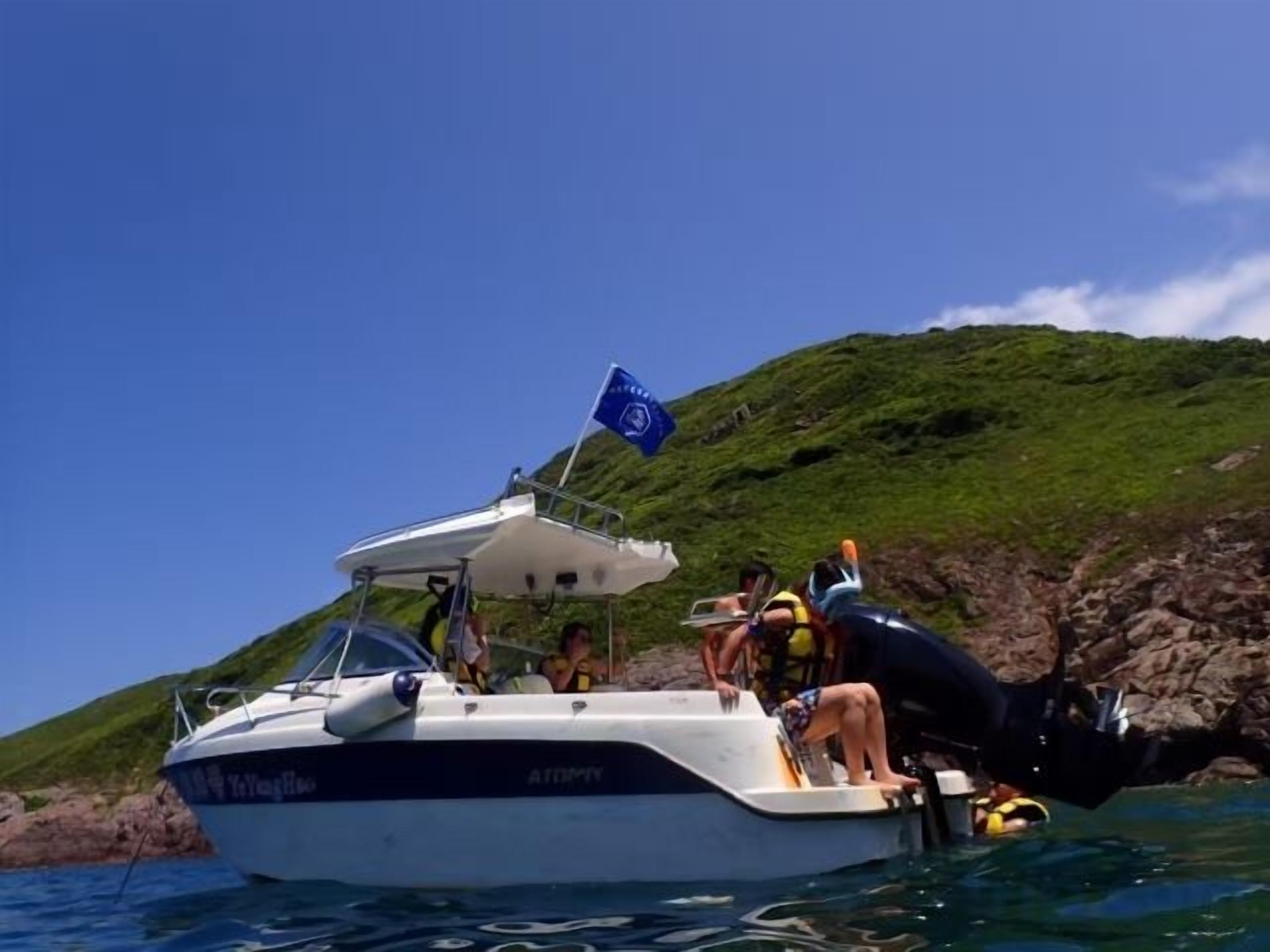 A boat with a flag, people on board, and a rocky shoreline in the background.
