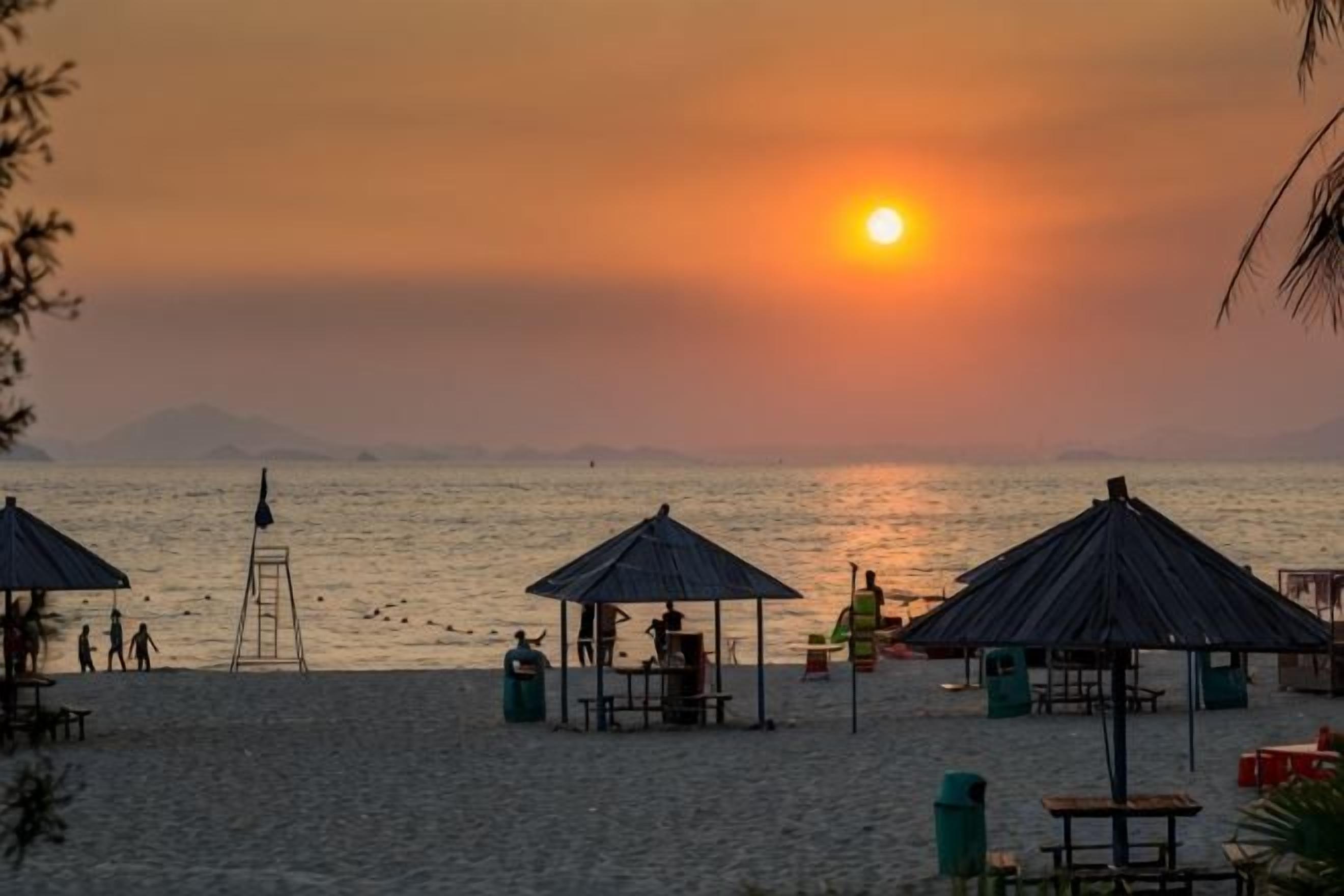 A beach with umbrellas and a lifeguard tower.