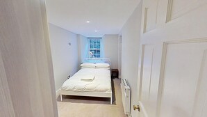 Ein schmaler Raum mit weißen Wänden, einem Bett, einem Heizkörper und einem Fenster mit Blick.