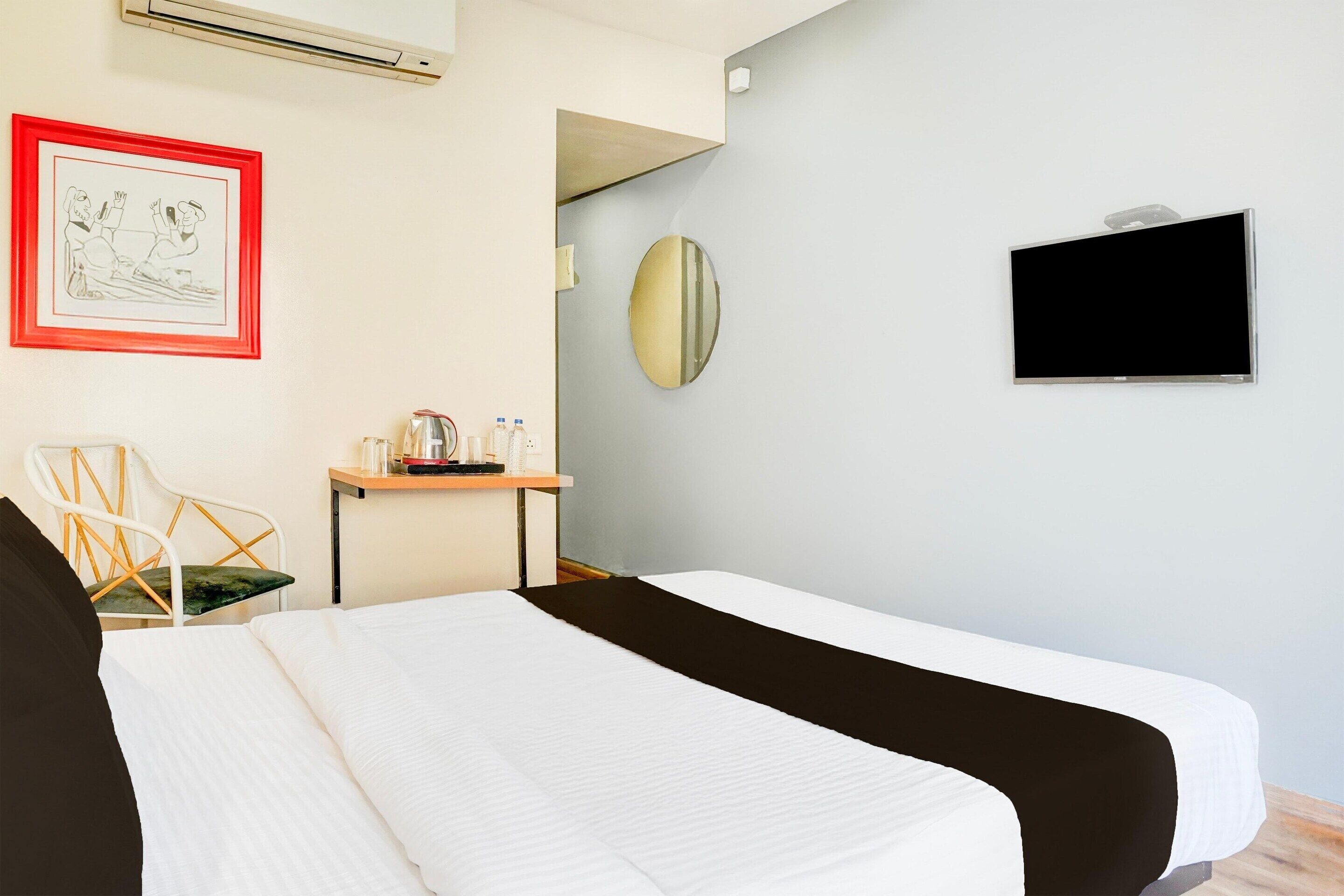 Une chambre d’hôtel avec deux lits, un bureau avec une chaise, un téléviseur à écran plat, un tableau encadré et un miroir.