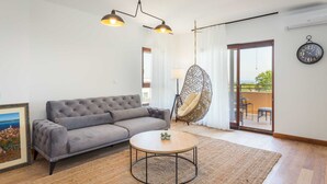 A living room with a grey sofa, a round coffee table, a hanging chair, and a view through a glass door. - 4 Guests Apartment in Medulin (Liznjan)