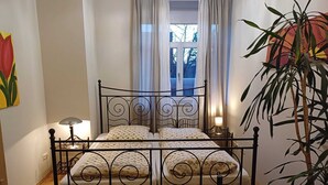 A bed with a metal frame, a bedside lamp, and a window with curtains. - Large vacation apartment in Nuremberg with good connections: Center, trade fair, Playmobil (Nürnberg)