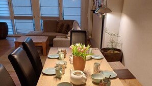 A dining table set with various dishes and a vase of flowers, surrounded by chairs and a sofa in a well-lit room with large windows. - Large vacation apartment in Nuremberg with good connections: Center, trade fair, Playmobil (Nürnberg)