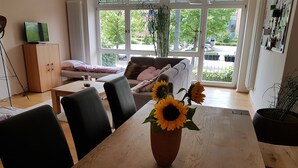 A dining area with a wooden table, black chairs, and a vase of sunflowers. There is a sofa with cushions and a television on a cabinet. - Large vacation apartment in Nuremberg with good connections: Center, trade fair, Playmobil (Nürnberg)
