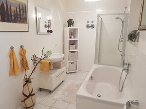 A modern bathroom with a white sink, a bathtub, and a shower. There are towels hanging on the wall, a small cabinet with baskets, and a decorative plant. - Spacious vacation apartment in Nuremberg with great access to the city center, the trade fair grounds, and Playmobil (Nürnberg)