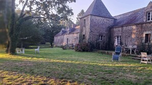 Um edifício de pedra com uma torre, um gramado e área externa com mesas e cadeiras.