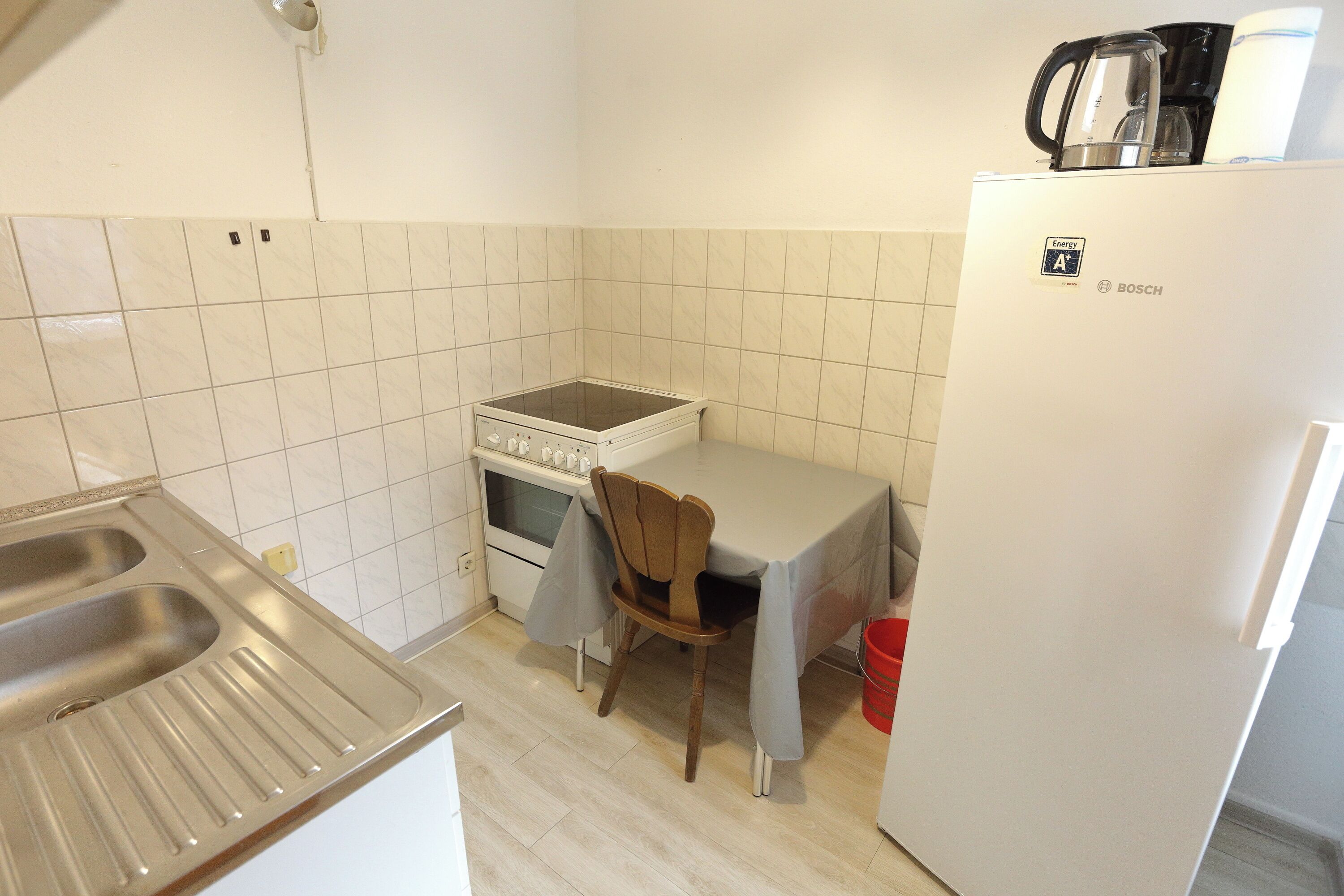 Una cocina compacta con estufa, lavamanos, una silla y refrigerador.