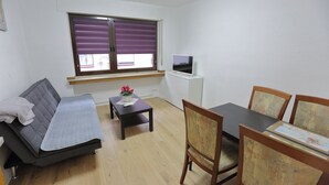 Un petit salon comprenant un canapé, une table, un téléviseur et un coin repas avec des chaises.