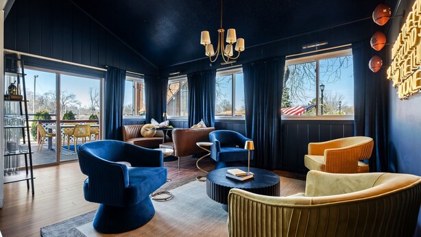 A modern living room with dark blue walls, a chandelier, and large windows.