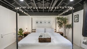 A neatly arranged bedroom with a four-poster bed, a bedside plant, and string lights.