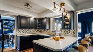 A modern kitchen with dark cabinets, a large island, and a dining area with velvet chairs.