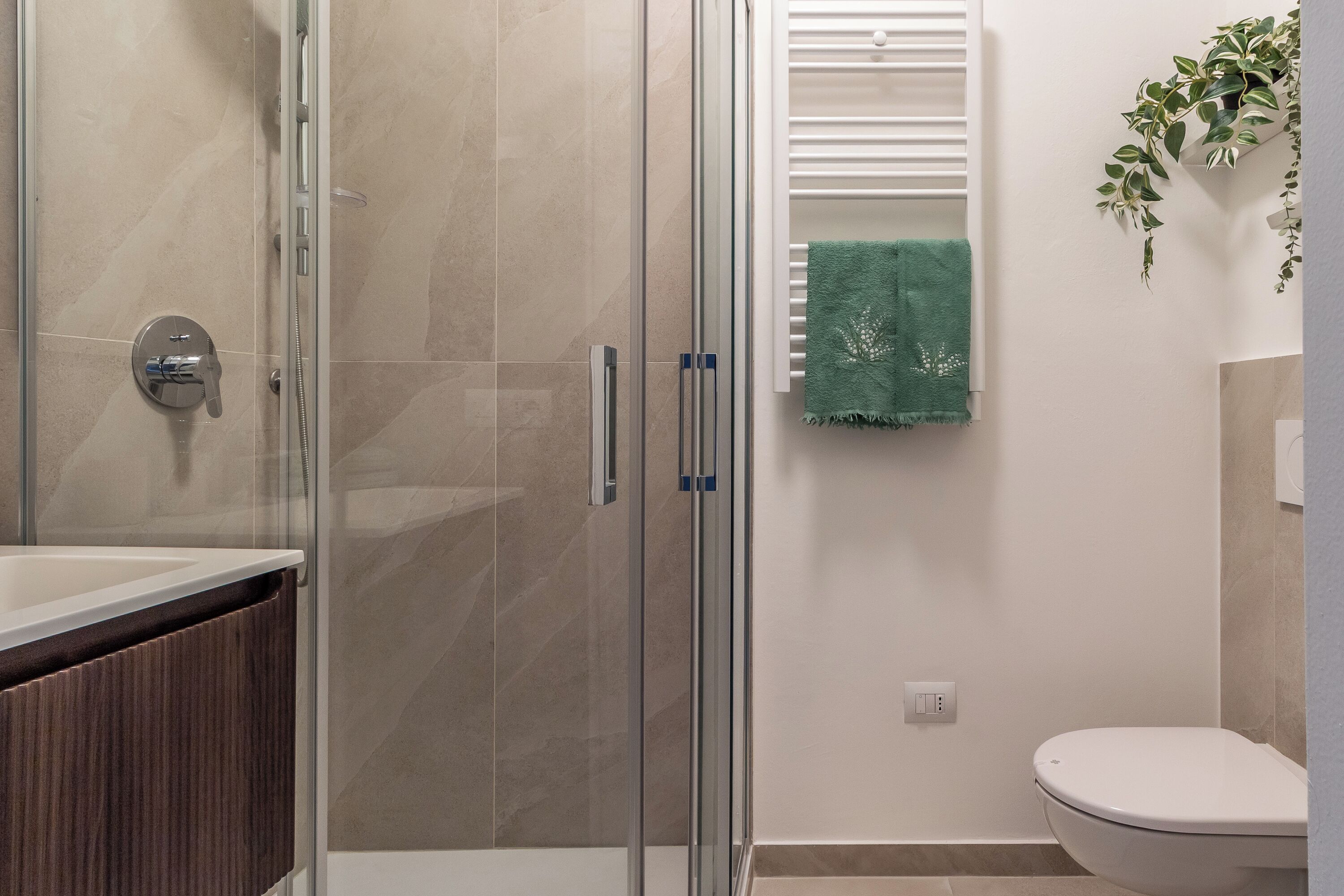A modern bathroom with a glass shower enclosure, a white toilet, and a green towel hanging on the wall.
