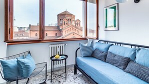 Un balcón con vistas a un edificio histórico, un sofá azul, una mesita con un cuenco y una lámpara.