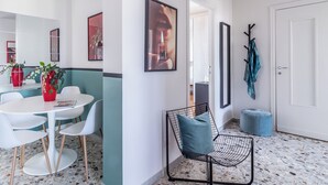 Un interior moderno con una mesa de comedor redonda, sillas blancas, una silla de alambre negra, un otomano azul y una puerta con perchero.
