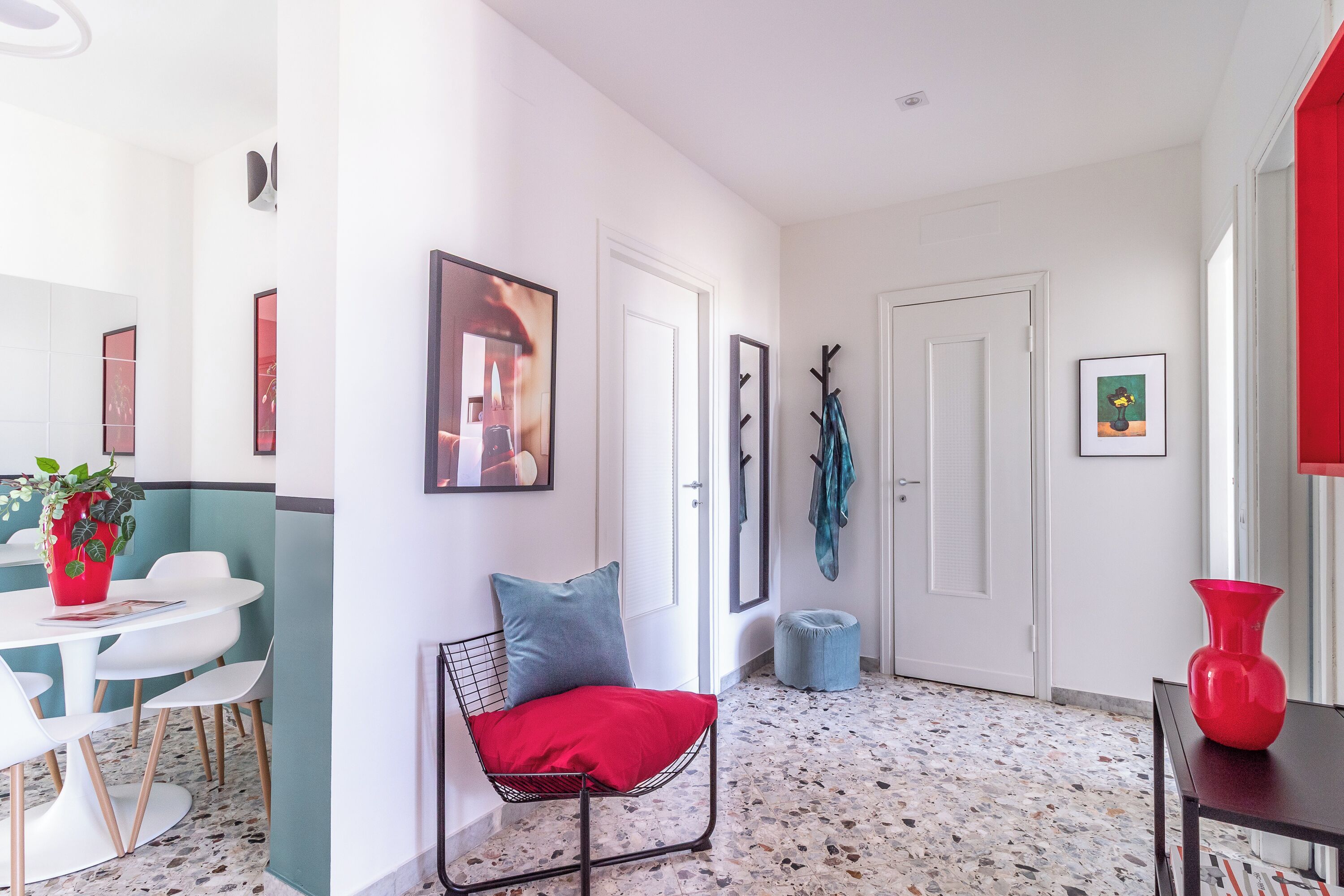 A modern interior with a dining area, a seating area with a red cushion, and a hallway with doors and artwork.