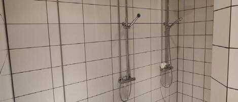 A bathroom with white tiled walls and a shower area with two showerheads and a handheld showerhead.