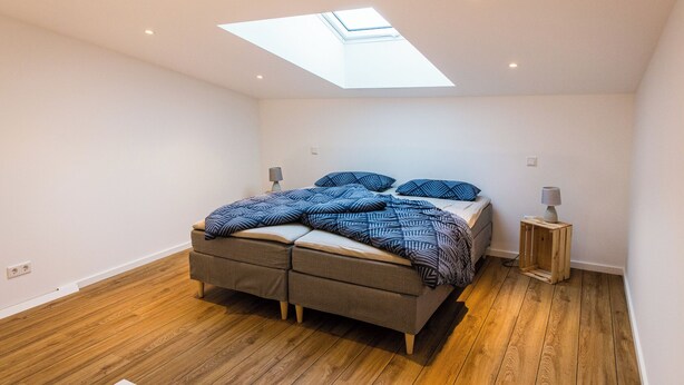 A bedroom with a skylight, a bed with patterned bedding, two bedside tables, and a wooden floor. - Vacation apartment in Hövelhof - 55sqm in a quiet location (Hövelhof)
