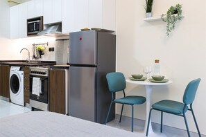 A compact kitchen with a refrigerator, oven, microwave, and washing machine. There is a dining area with two chairs and a table.