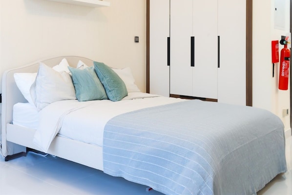 A neatly made bed with a white headboard, a blue-striped bedspread, and multiple pillows in various shades.
