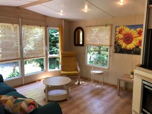 Quarto com janelas amplas, uma poltrona amarela, uma mesa redonda e uma pintura de girassóis.