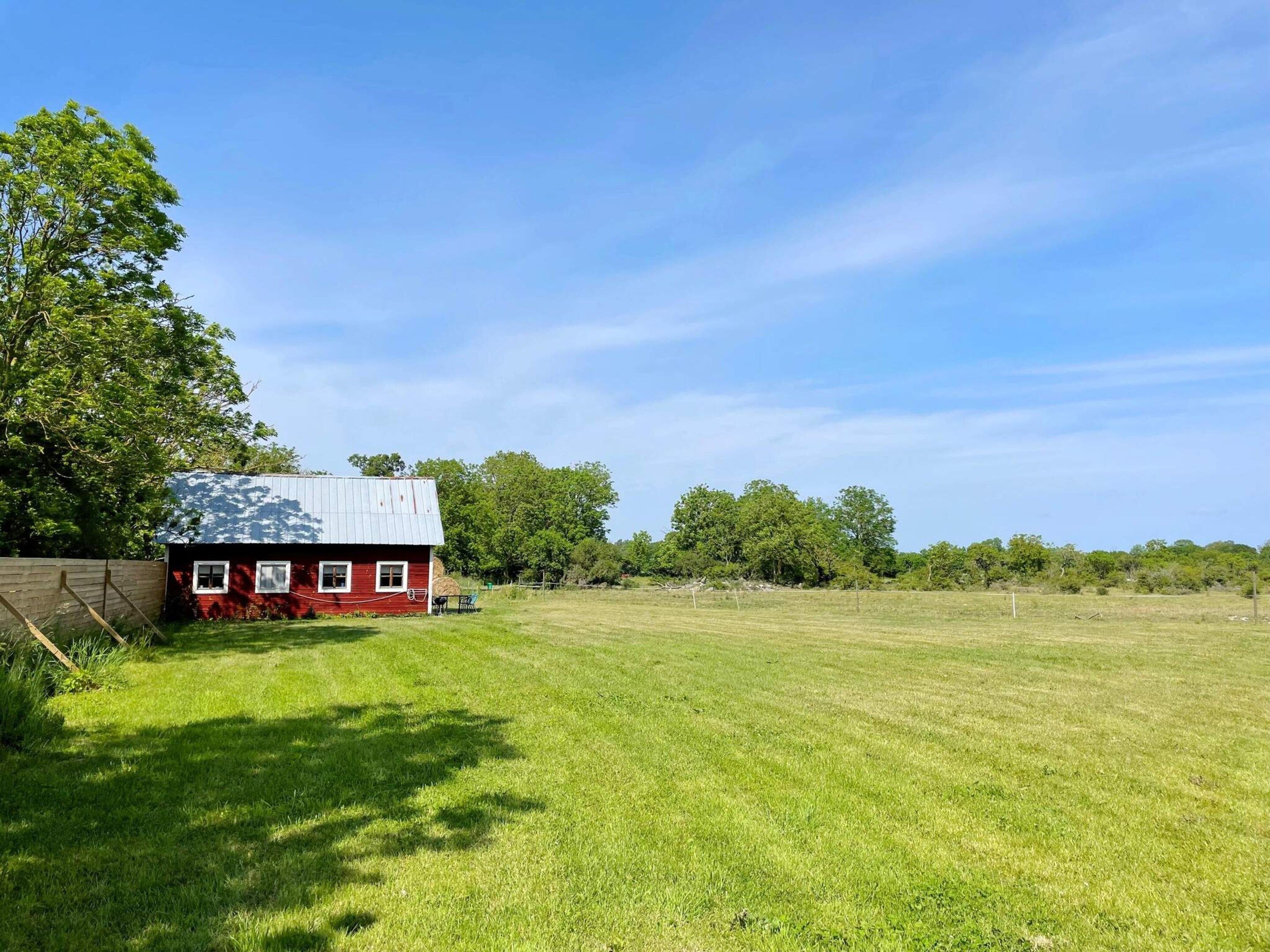 A red barn with a metal roof, surrounded by a grassy field and trees.