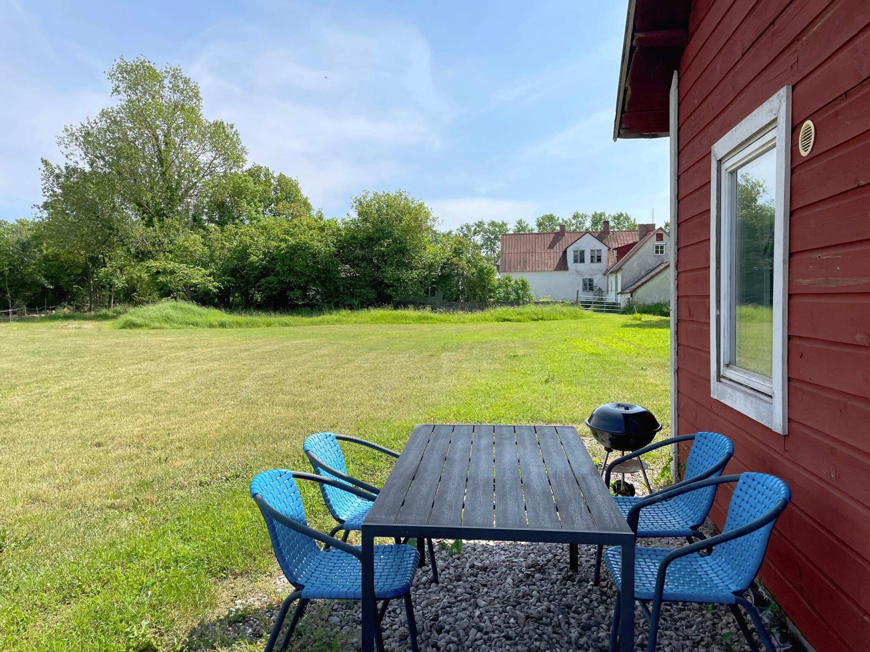 A patio with a table and chairs, a red building, and a grassy yard with trees.