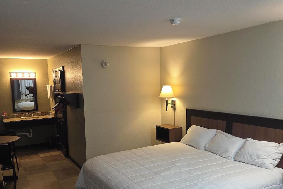 Habitación de hotel con cama, escritorio, espejo y mesita de noche.