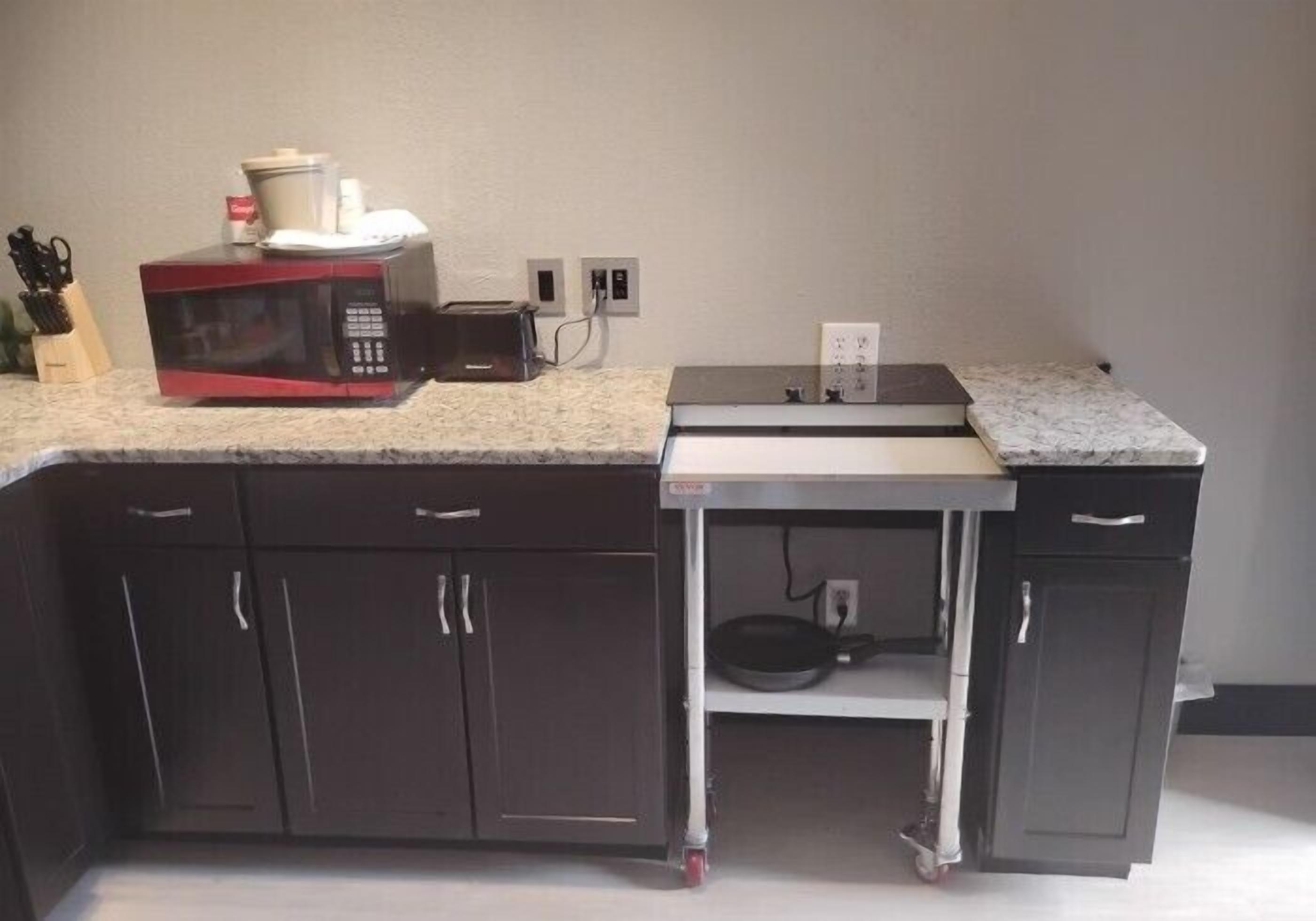 A compact kitchen with dark cabinets, a microwave, a small table, and a toaster.
