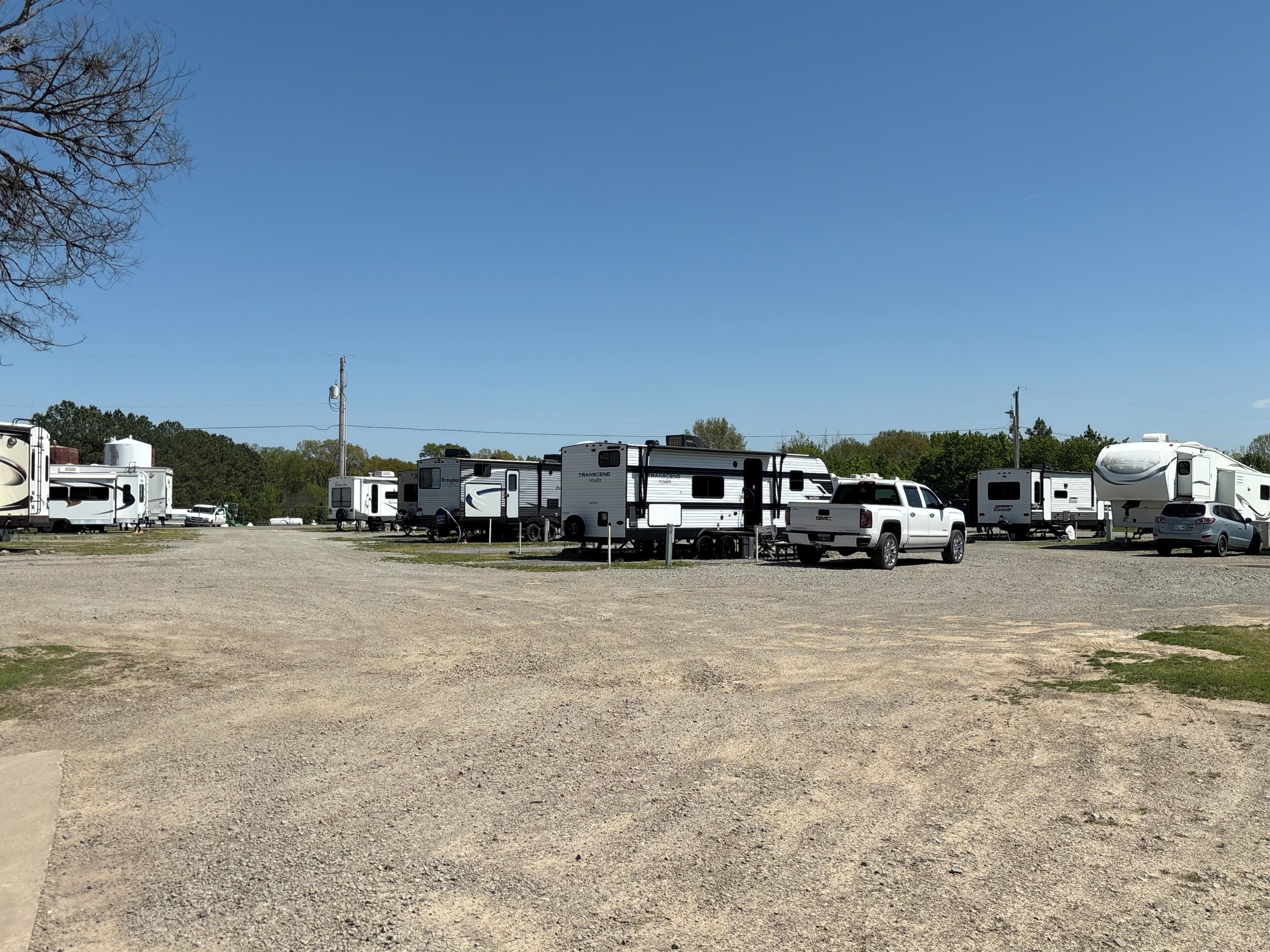 Un espace de stationnement recouvert de gravier, où sont garés plusieurs camping-cars et un camion GMC blanc.