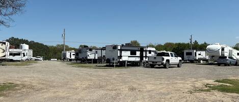 Un espace de stationnement recouvert de gravier, où sont garés plusieurs camping-cars et un camion GMC blanc.