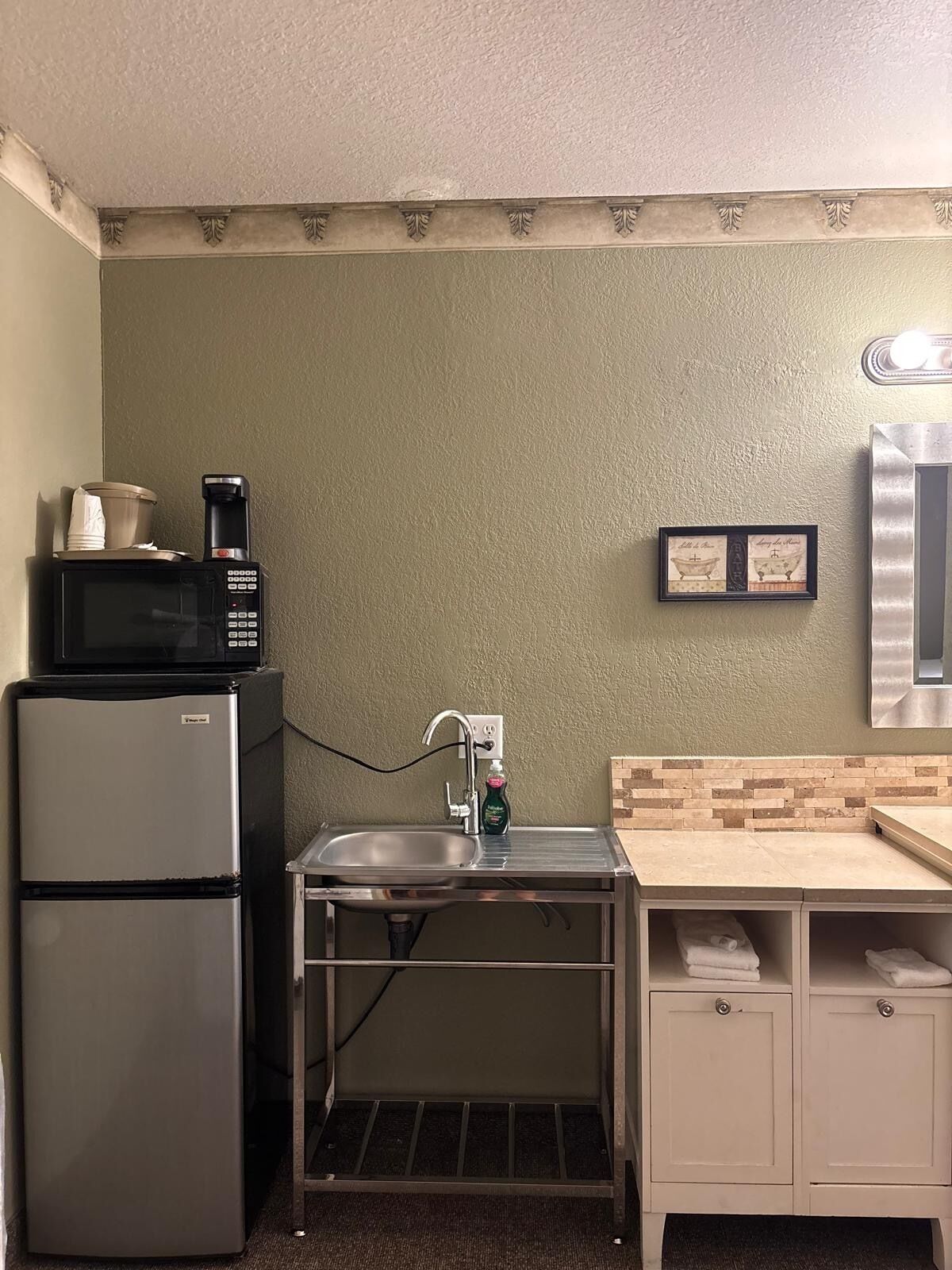 A compact kitchenette with a refrigerator, microwave, sink, and a small countertop.