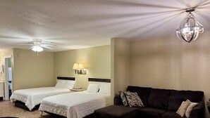Una habitación de hotel con dos camas, un sofá marrón oscuro, una mesita y un ventilador de techo.
