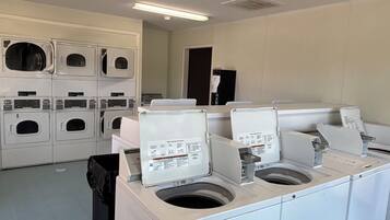 A laundry room with multiple washing machines and dryers, a trash bin, and a door in the background.