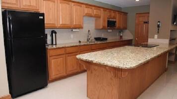 A kitchen with wooden cabinets, a black refrigerator, granite countertops, and a microwave.