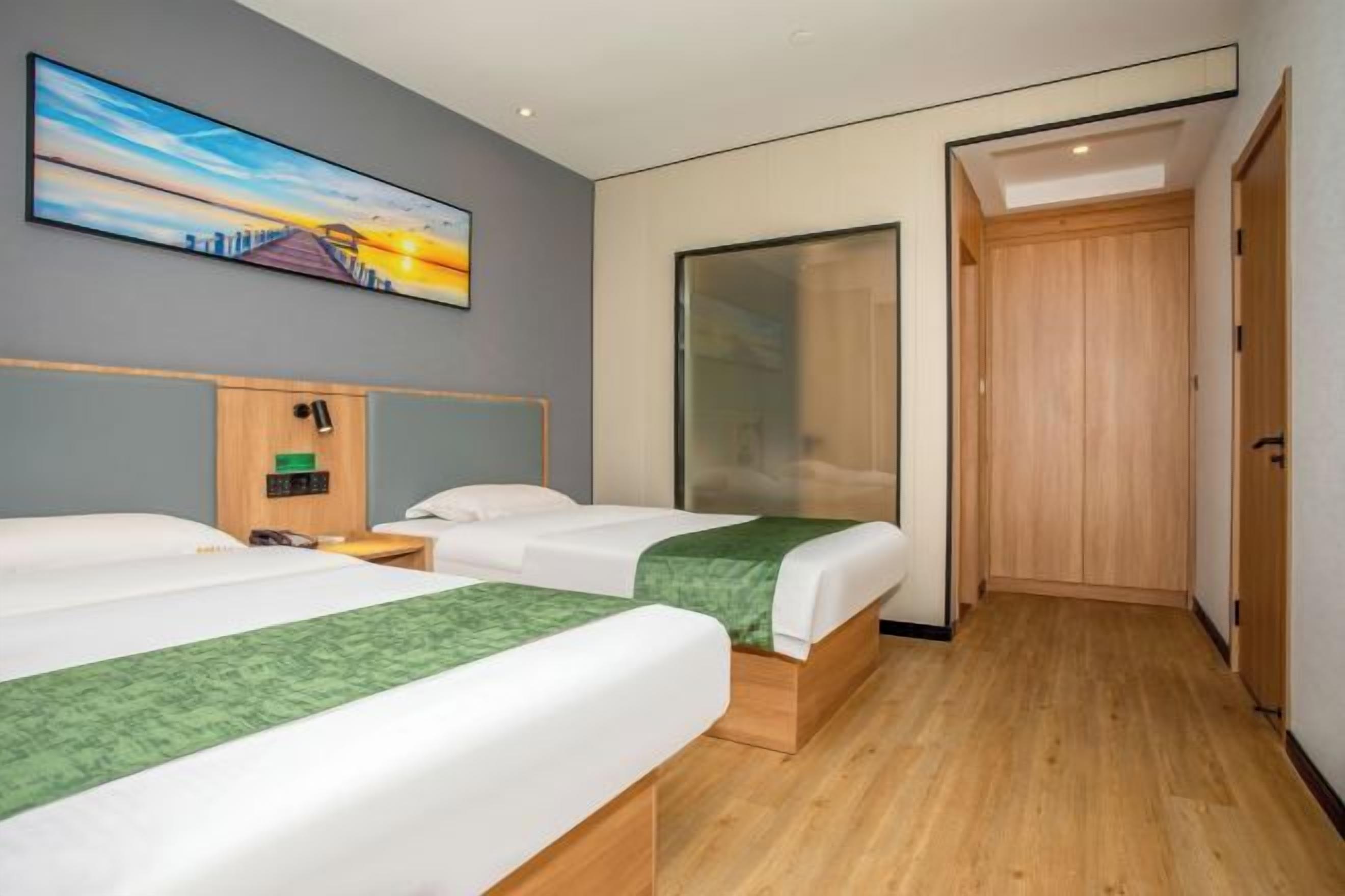 Habitación de hotel con dos camas, un armario de madera, un cuadro en la pared y una puerta que da a otra habitación.