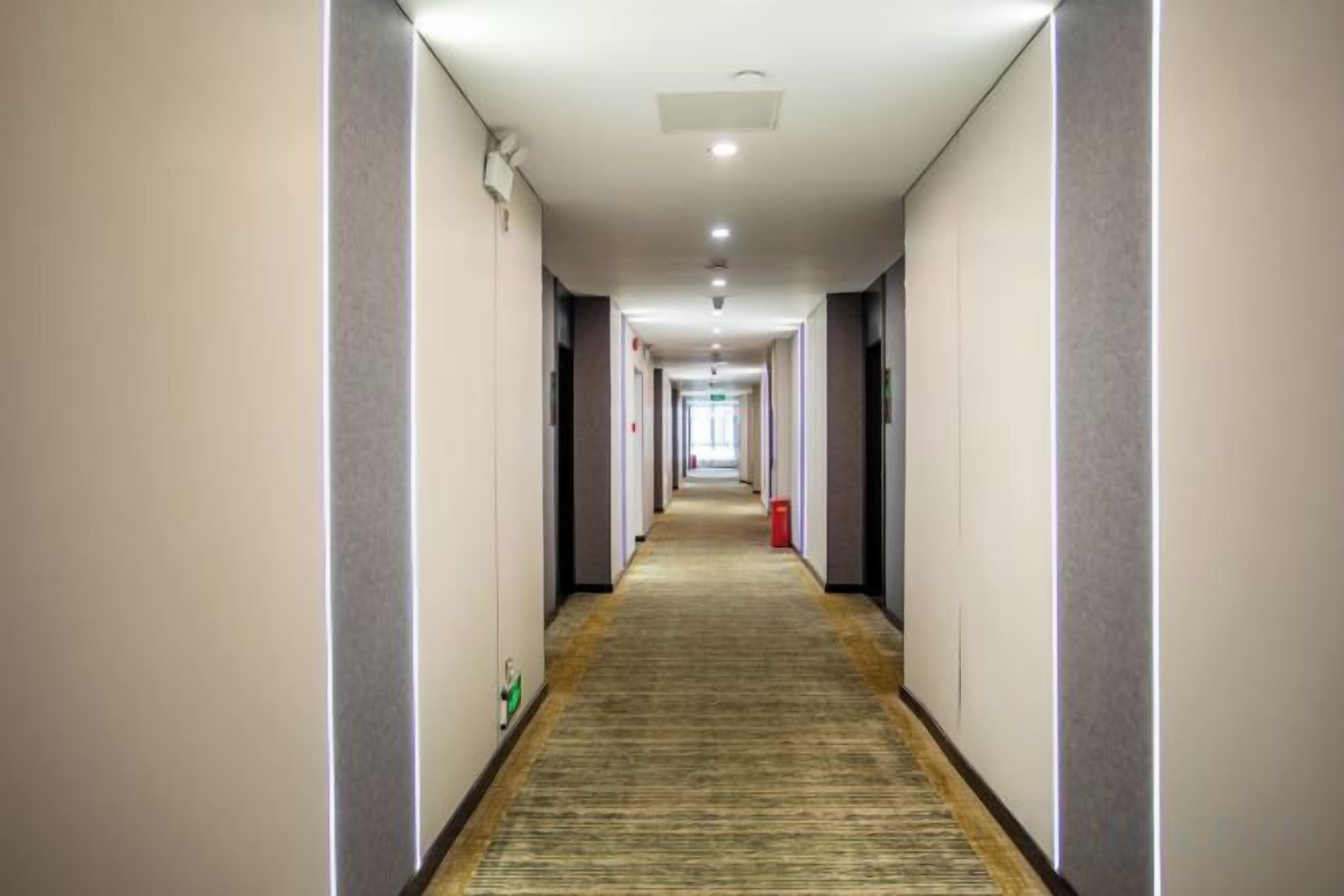 Corredor de hotel com piso coberto por carpete, paredes de cor clara e teto com iluminação embutida.