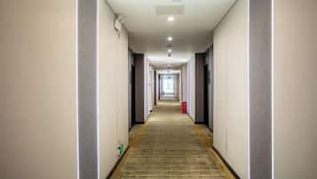 Corredor de hotel com piso coberto por carpete, paredes de cor clara e teto com iluminação embutida.