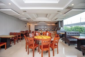 A restaurant with round tables and chairs, a kitchen in the background, and a view of greenery outside. - GreenTree Inn (Shanghai Fengxian Xidu) (Shanghai)