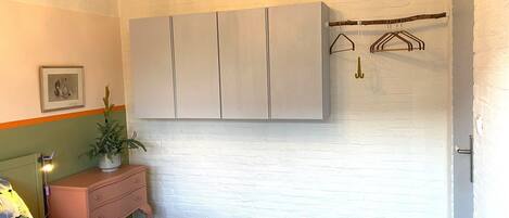 A bedroom with a bed, a dresser, a wardrobe, a plant, and a coat rack.