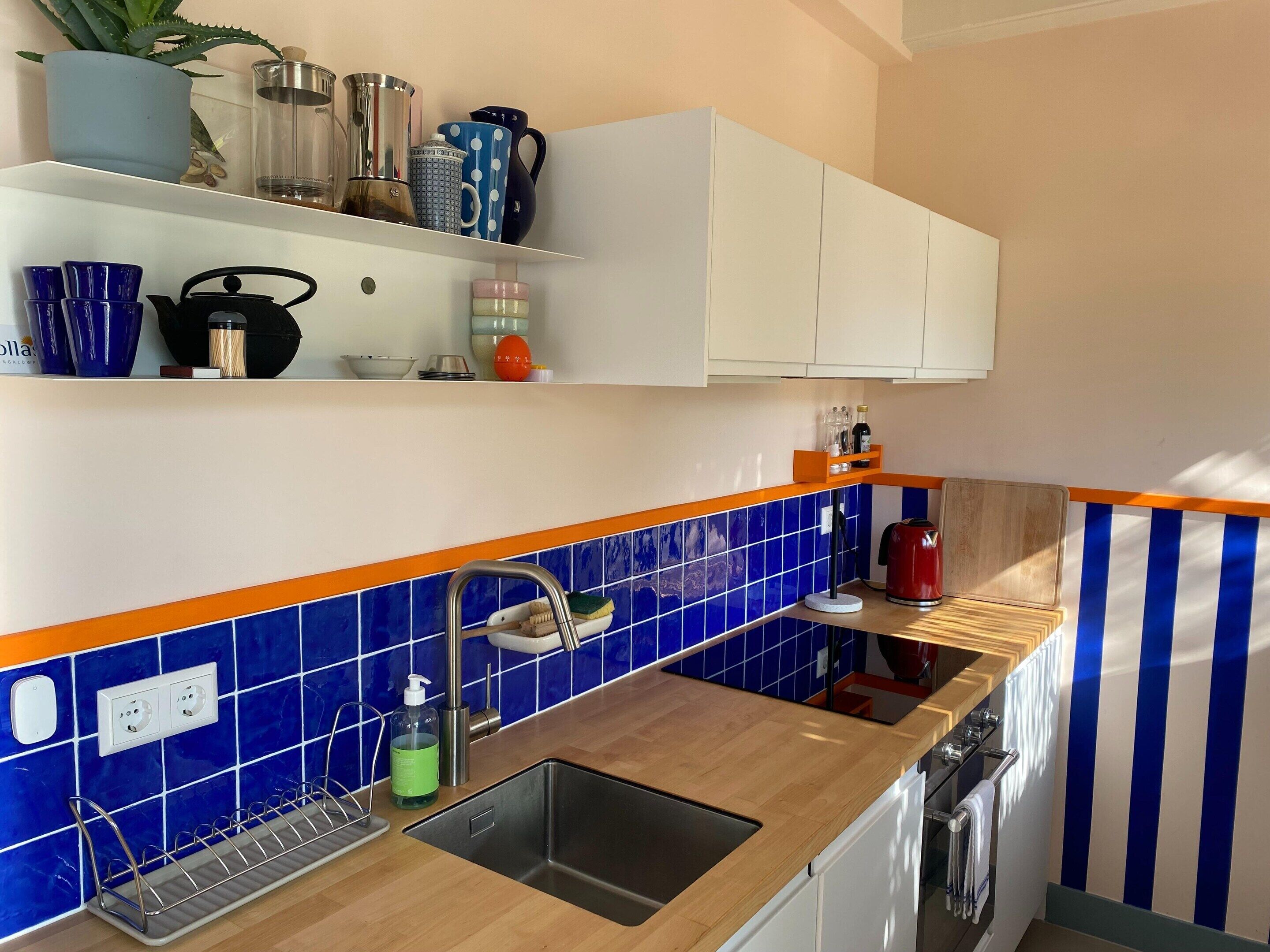 A modern kitchen with blue and orange tiles, stainless steel appliances, and a wooden countertop.