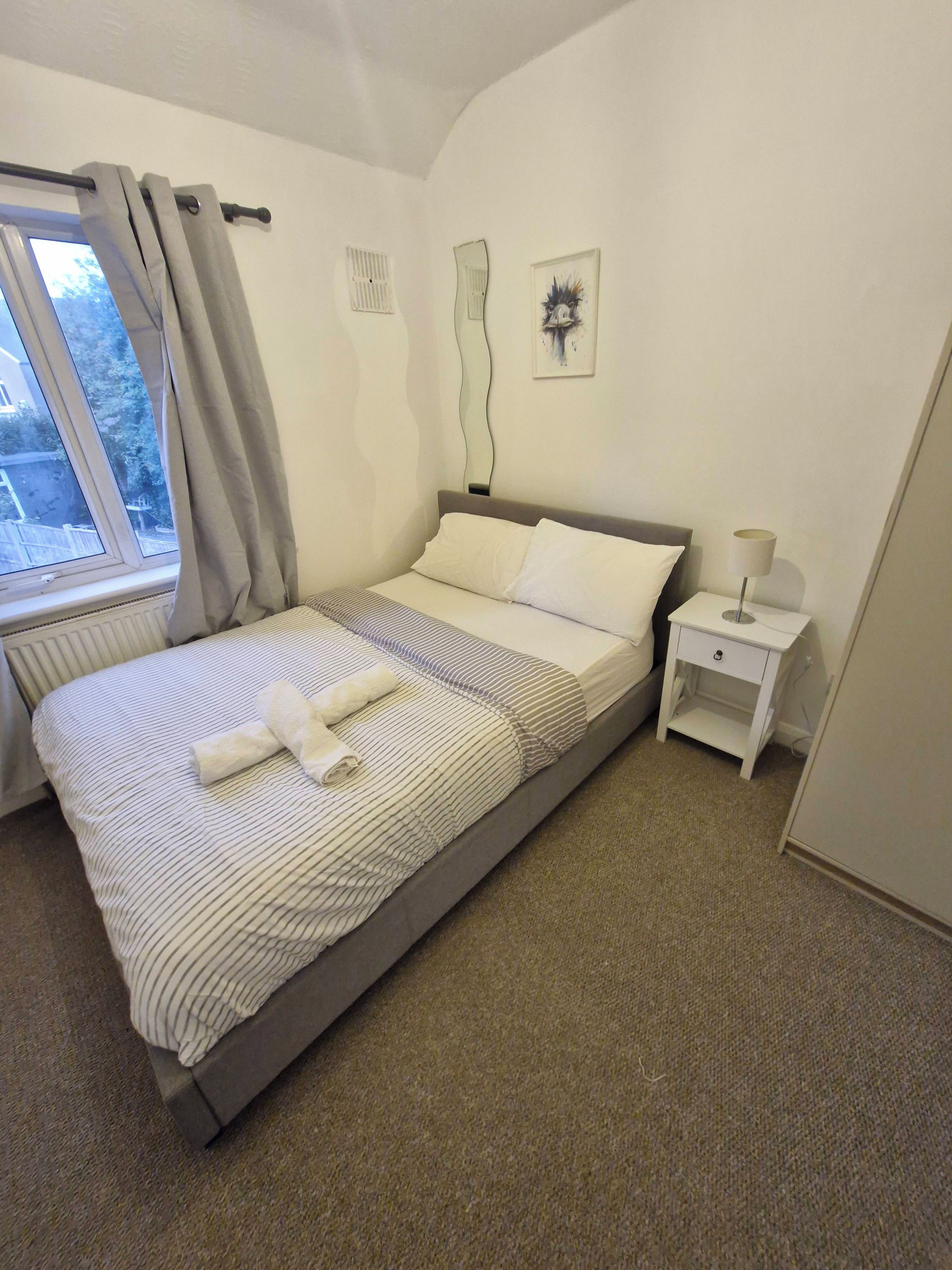 A neatly made bed with a striped bedspread and pillows, a bedside table with a lamp, and a window with curtains.